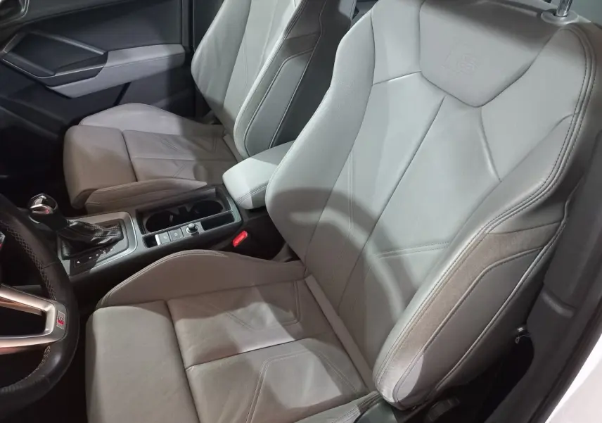 Vue intérieure côté conducteur de l'Audi Q3 blanc, sièges sport en cuir gris avec logo S embossé.
