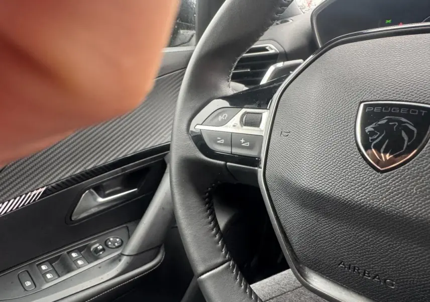 Gros plan sur le volant cuir noir du Peugeot 2008 Hybrid 145 Allure 2025 avec commandes intégrées et logo lion chromé.