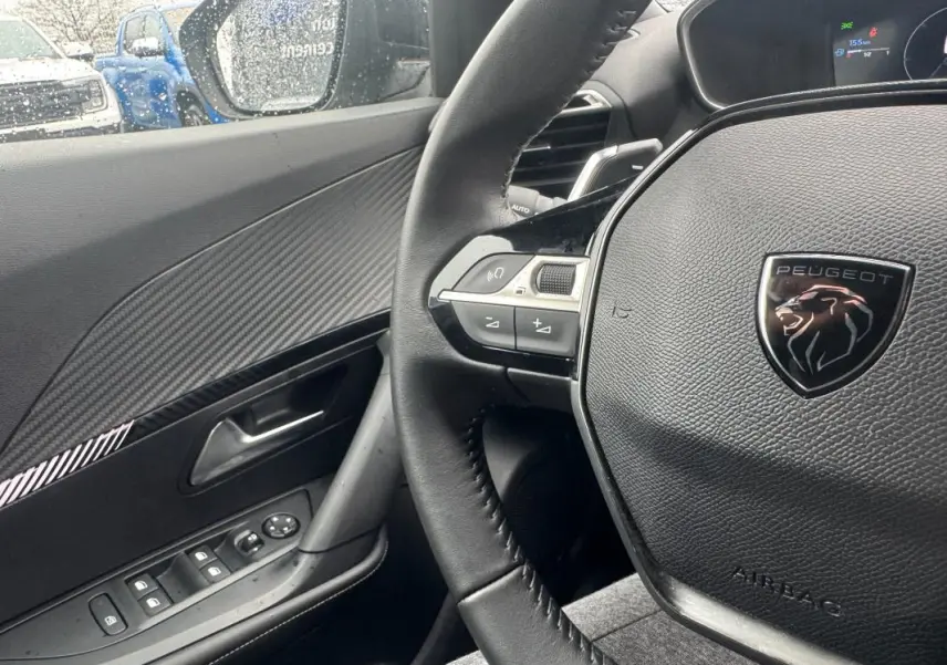 Vue intérieure côté conducteur du Peugeot 2008 gris 2025, volant cuir avec logo lion et commandes intégrées.