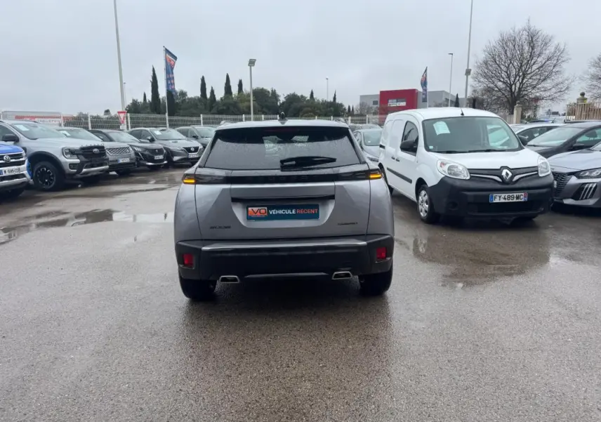 Vue arrière d’un Peugeot 2008 gris avec feux LED allumés, garé sur un parking humide entouré d’autres véhicules.