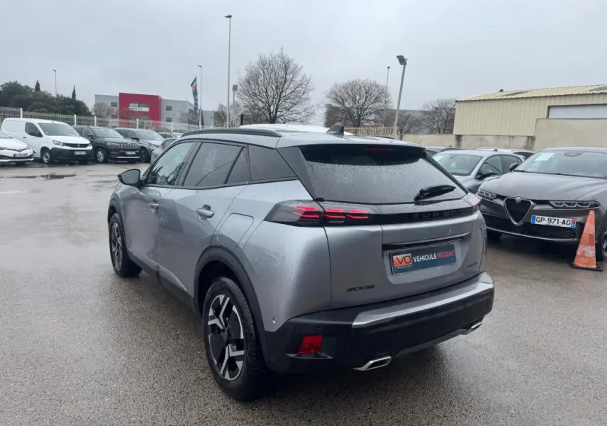 Vue 3/4 arrière gauche d’un Peugeot 2008 Hybrid gris avec jantes alliage 17 pouces et barres de toit visibles par temps humide.