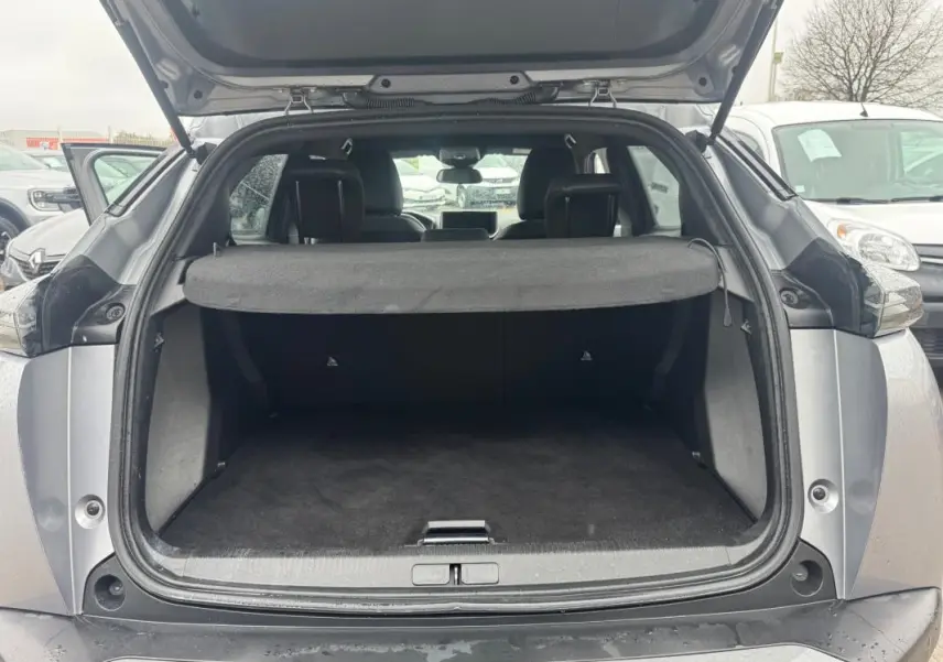 Coffre ouvert vu de l'arrière d'un Peugeot 2008 gris 2025, avec cache-bagages et intérieur sombre visible.