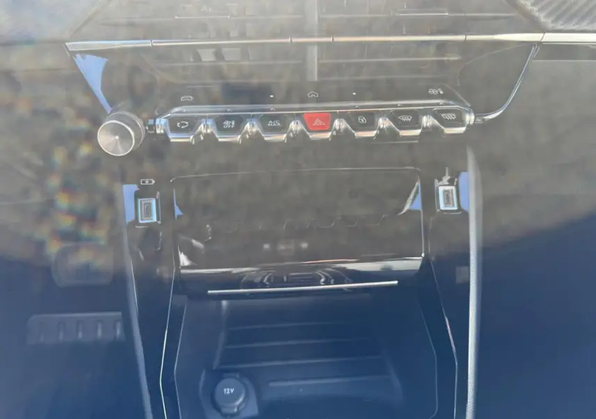 Vue rapprochée de la console centrale du Peugeot 2008 Hybrid 136 Allure 2025 noire, avec boutons de commande et prise 12V.