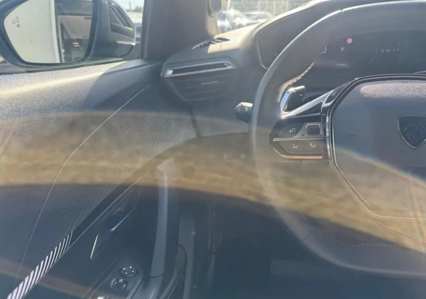 Vue intérieure côté gauche du Peugeot 2008 Hybrid 136 Allure 2025 noir, avec volant multifonction et commandes sur porte.