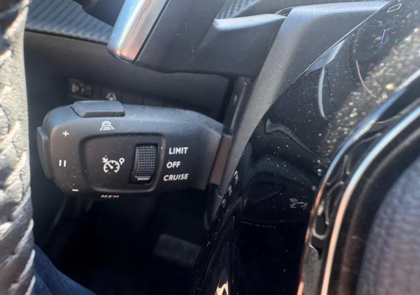 Gros plan sur la commande de régulateur de vitesse à gauche du volant dans l’habitacle noir du Peugeot 2008 Hybrid 136 Allure.