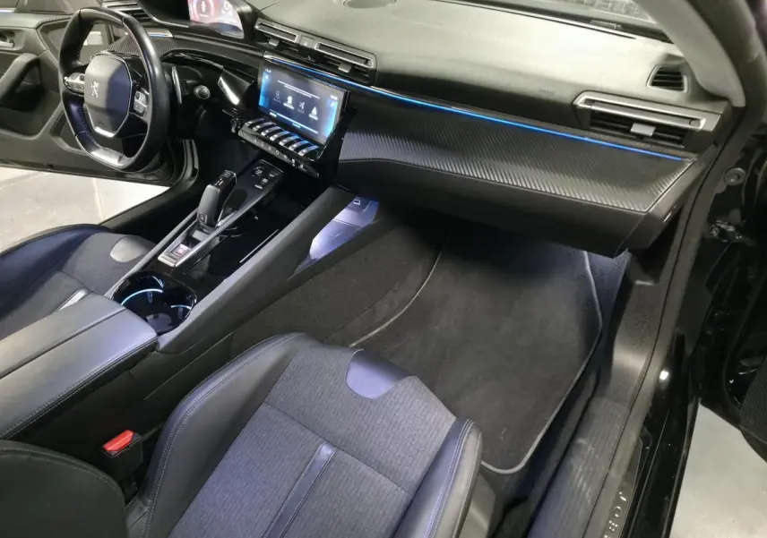 Vue intérieure côté passager de la Peugeot 508 SW noire, avec tableau de bord carbone et éclairage d'ambiance bleu.