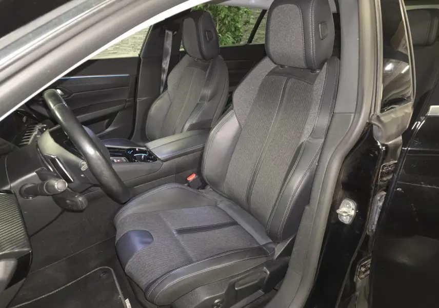 Vue intérieure côté conducteur de la Peugeot 508 SW noire, mettant en valeur les sièges tissu et cuir avec surpiqûres grises.