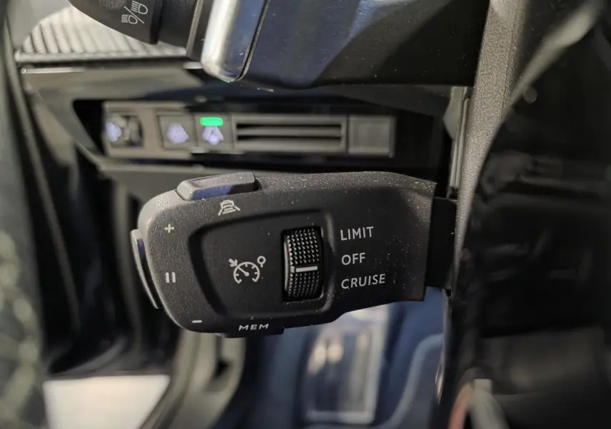 Gros plan sur la commande de régulateur de vitesse au volant d’une Peugeot 508 SW noire, intérieur sombre.