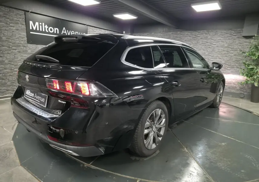 Peugeot 508 SW noire vue 3/4 arrière droit, avec feux arrière allumés et barres de toit aluminium.