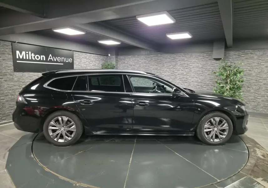 Profil droit d'une Peugeot 508 SW noire 2019 en stationnement intérieur avec barres de toit et jantes alliage 17 pouces.