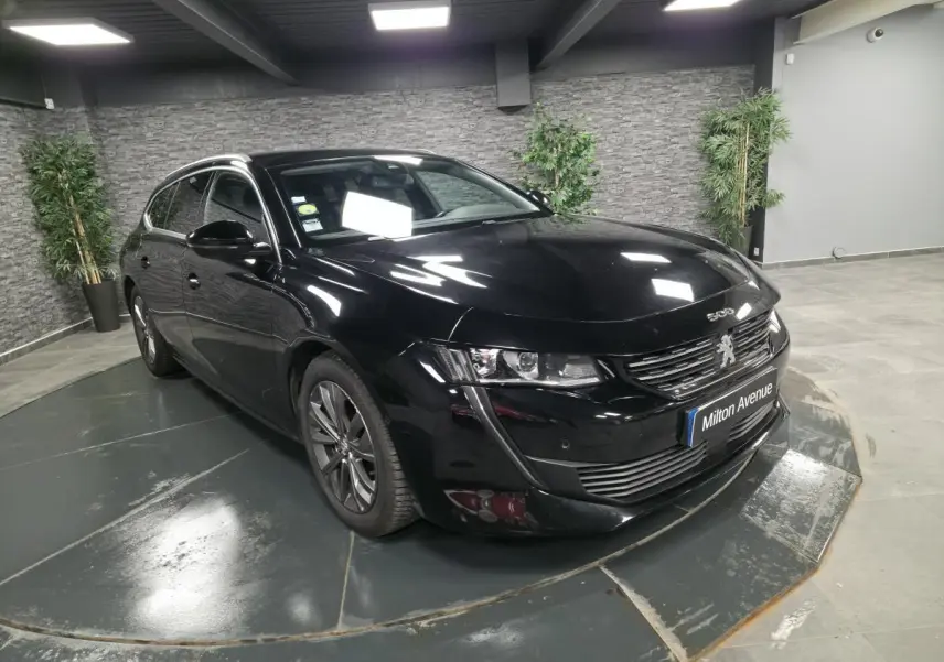 Peugeot 508 SW noire vue 3/4 avant droit avec calandre chromée et barres de toit aluminium en intérieur showroom.