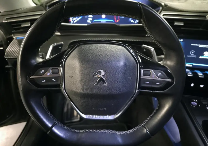 Vue rapprochée du volant cuir noir du Peugeot 508 SW 2019, avec commandes intégrées et tableau de bord numérique en arrière-plan.