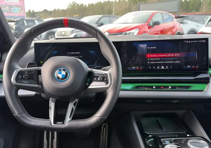 Vue intérieure frontale du tableau de bord et volant noir de la BMW Série 5 i5 M60 avec écran large et insert vert.