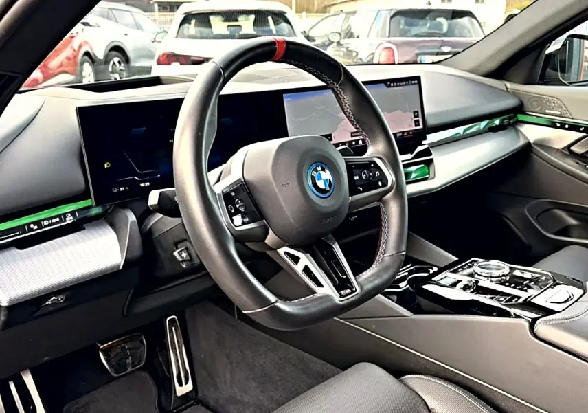 Vue intérieure côté conducteur de la BMW Série 5 i5 M60 2024 avec volant sport, écran tactile et inserts verts lumineux.