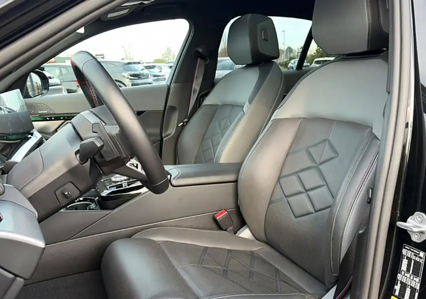 Vue intérieure côté conducteur de la BMW Série 5 i5 M60 2024 avec sièges en cuir noir et volant multifonction.