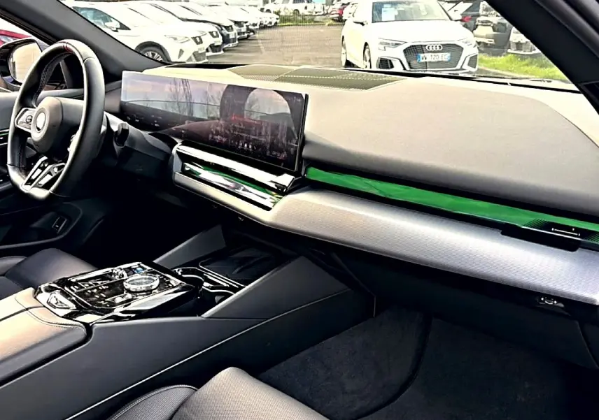 Vue intérieure côté conducteur de la BMW Série 5 i5 M60 2024, tableau de bord moderne avec écran large et finitions noires.
