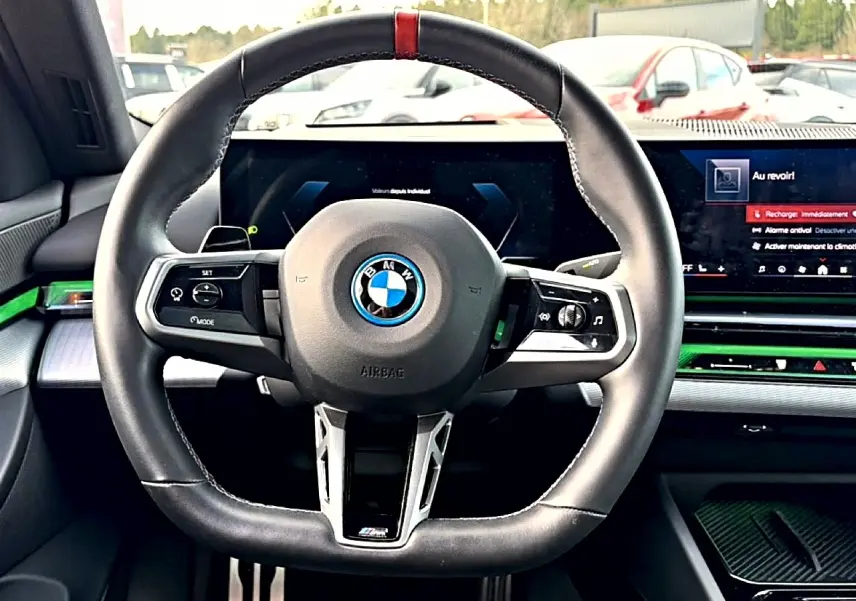 Vue intérieure centrée sur le volant sport noir avec surpiqûre rouge de la BMW Série 5 i5 M60 2024.
