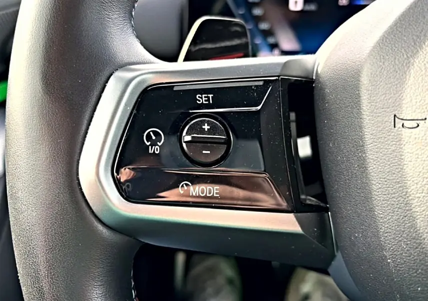 Gros plan sur les commandes de régulateur de vitesse à gauche du volant cuir noir d'une BMW Série 5 i5 M60 2024.