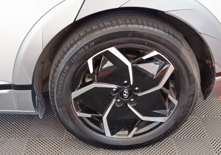 Gros plan sur la roue avant droite noire et argentée d'une Hyundai IONIQ beige, mettant en valeur la jante au design géométrique.