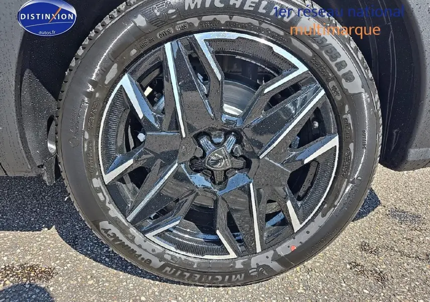 Gros plan sur la jante alu noire et argentée d'un Peugeot 5008 gris titane, avec pneu Michelin humide.