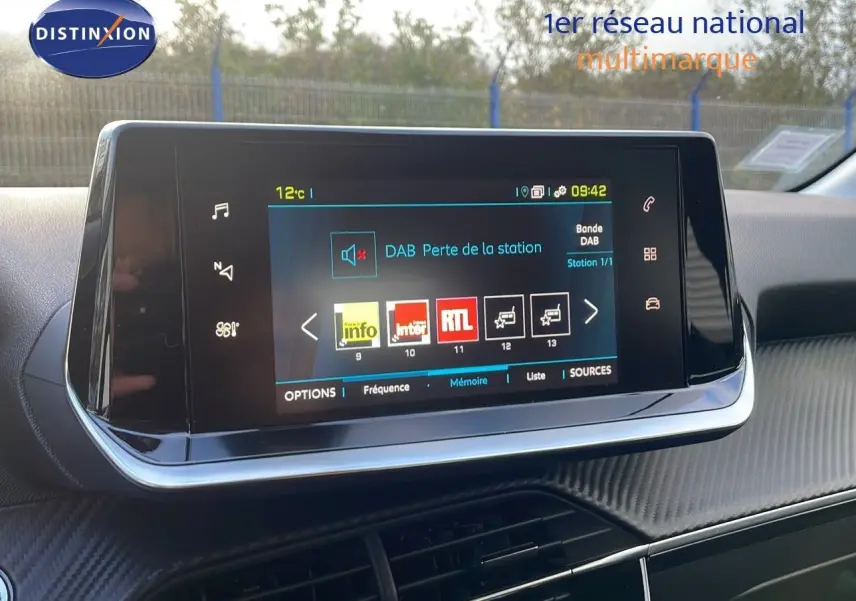 Écran tactile central du tableau de bord de la Peugeot 208 électrique gris Artense, affichant les stations radio numériques.