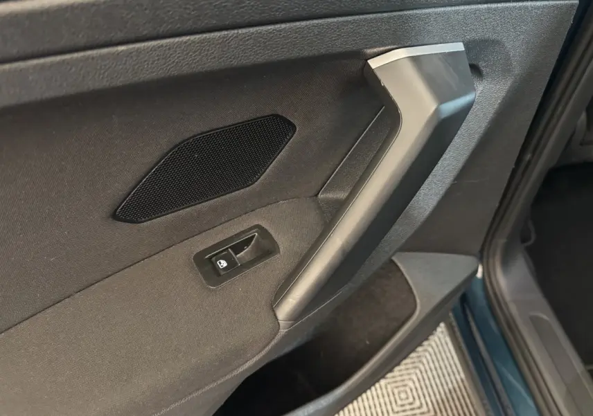 Gros plan sur la poignée intérieure et le bouton de verrouillage de la porte côté conducteur du Volkswagen Tiguan bleu.