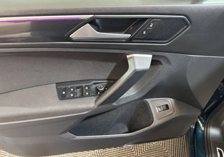 Vue rapprochée de la porte avant gauche du Volkswagen Tiguan bleu, montrant les commandes des vitres et la poignée intérieure.