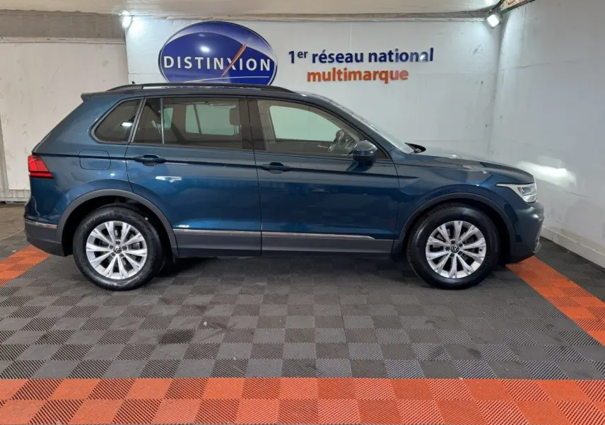 Vue latérale droite d'un Volkswagen Tiguan bleu 2021 avec rails de toit noirs dans un showroom.