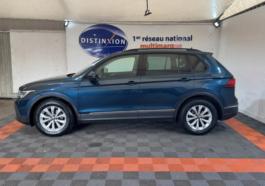 Vue de profil côté gauche d'un Volkswagen Tiguan bleu avec rails de toit noirs dans un showroom.