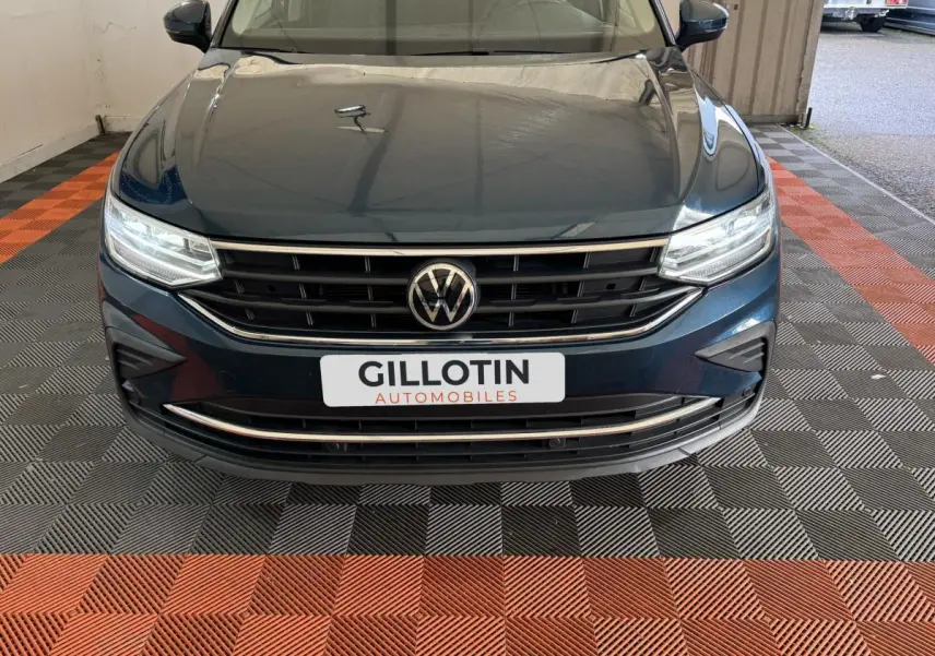 Vue avant frontale du Volkswagen Tiguan bleu avec calandre noire et phares LED allumés dans un garage.