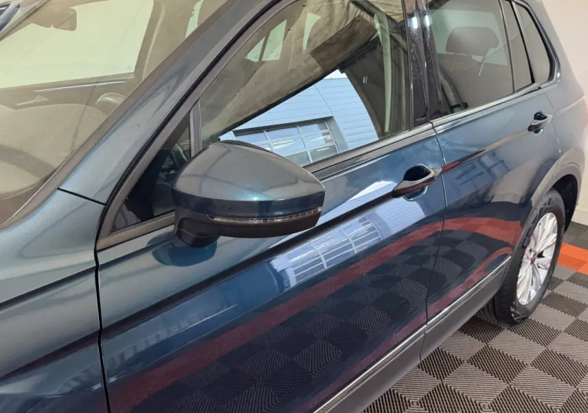 Vue latérale côté gauche du Volkswagen Tiguan bleu avec rétroviseur noir et jante visible sur sol damier.