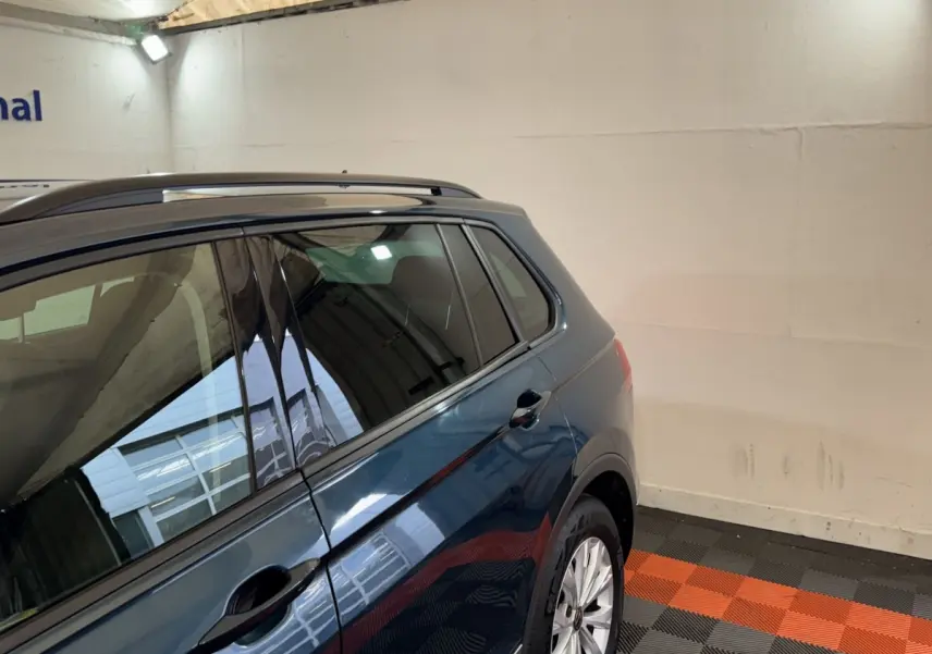 Vue 3/4 arrière droite du Volkswagen Tiguan bleu avec rails de toit noirs dans un garage.
