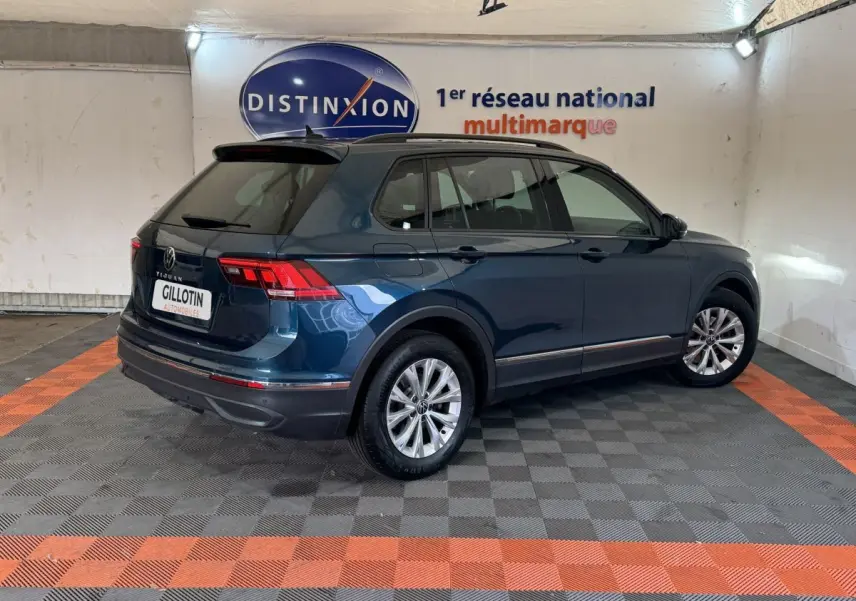 Vue 3/4 arrière droite d’un Volkswagen Tiguan bleu avec rails de toit noirs dans un showroom.