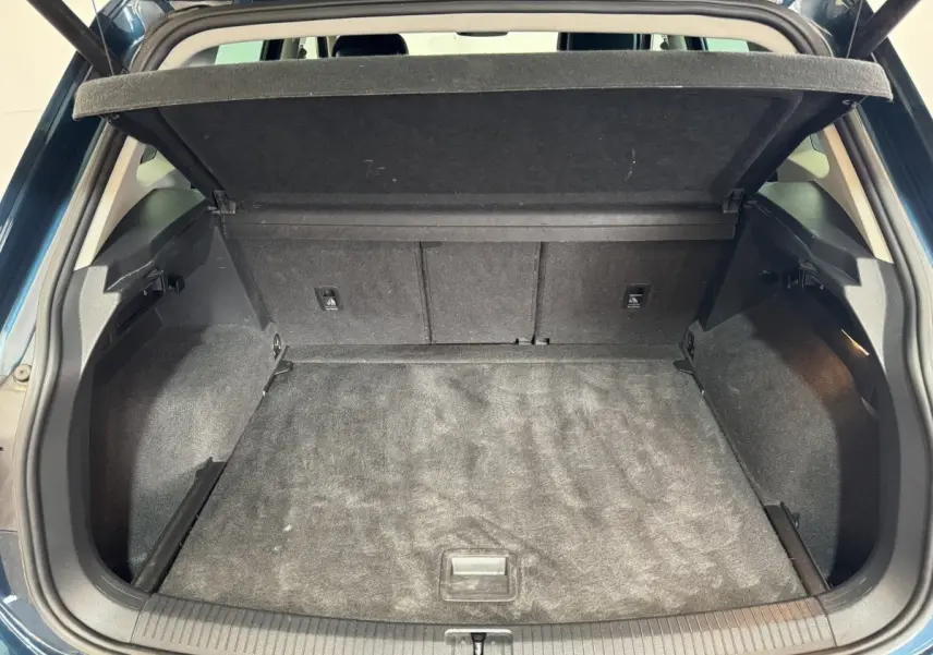 Coffre ouvert vu de l'arrière d'un Volkswagen Tiguan bleu 2021, avec cache-bagages relevé et intérieur noir.