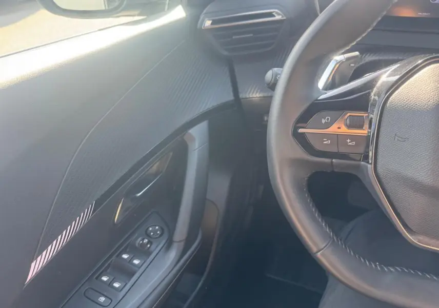 Vue intérieure côté gauche du Peugeot 2008 Hybrid 145 Allure 2025, montrant la portière et le volant avec commandes intégrées.