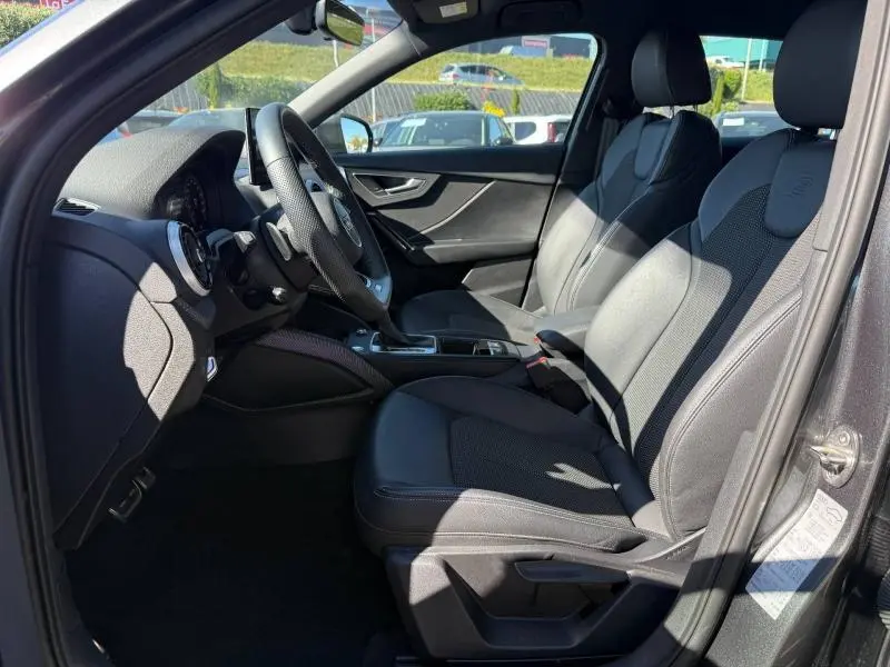 Vue intérieure côté conducteur de l'Audi Q2 35 TDI S line 2025, sièges sport en cuir noir avec volant multifonction.