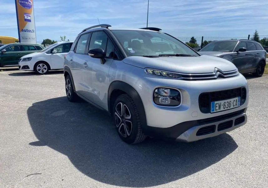 Vue 3/4 avant d'un Citroën C3 Aircross gris Artense avec toit noir et jantes distinctives, stationné en extérieur.