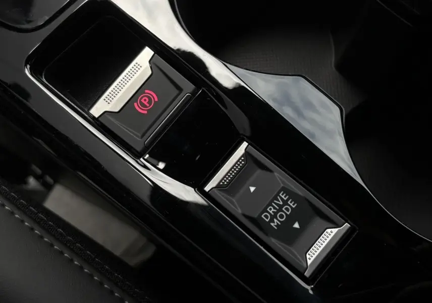 Gros plan sur la console centrale noire brillante de la Peugeot 208 Hybrid avec bouton frein électrique et sélecteur Drive Mode.