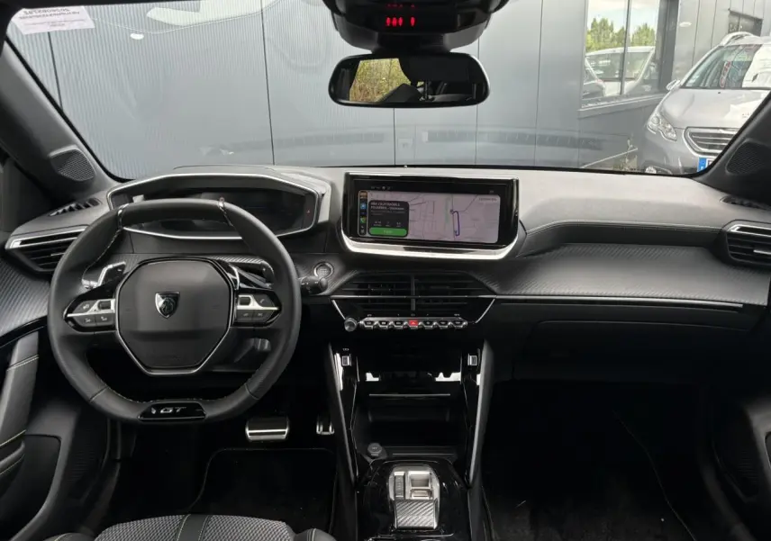 Vue intérieure avant du Peugeot 208 Hybrid GT 2025 avec tableau de bord noir, volant compact GT et écran tactile central.