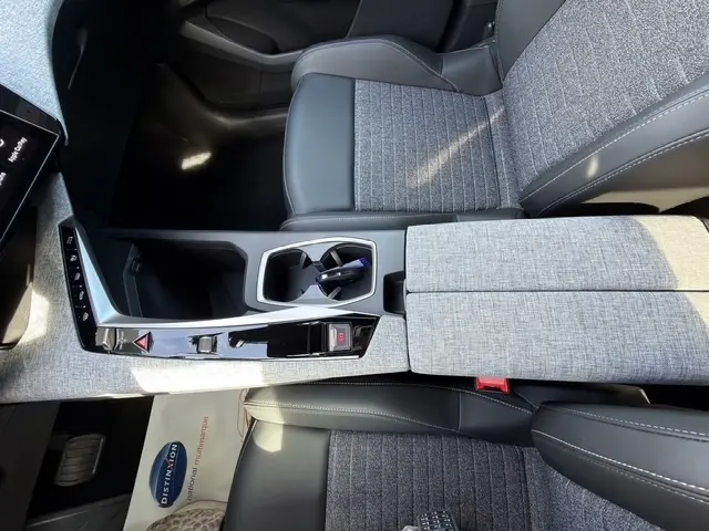 Vue intérieure rapprochée du poste de conduite et console centrale grise avec sièges tissu et cuir noir du Peugeot 5008 hybride 2025.