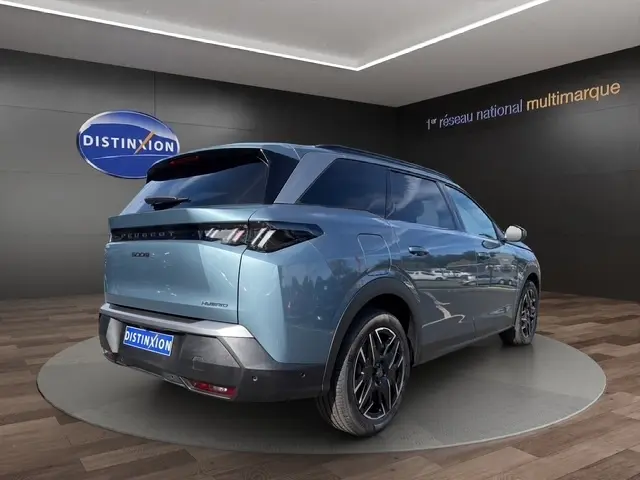 Vue 3/4 arrière droite d'un Peugeot 5008 bleu hybride 2025 avec feux LED et jantes noires en showroom.