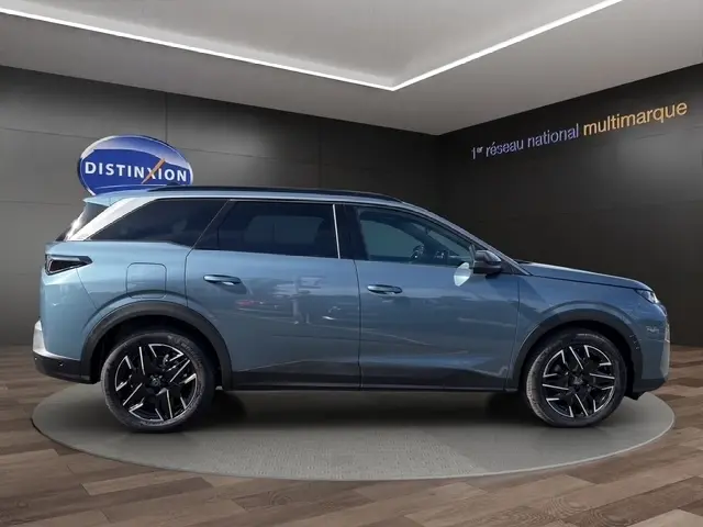 Vue de profil droit du Peugeot 5008 bleu hybride 2025 dans un showroom avec jantes noires distinctives.