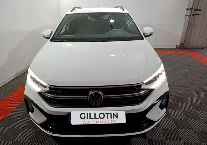 Vue frontale d'un Volkswagen Taigo blanc avec phares LED allumés et calandre R-Line dans un showroom.