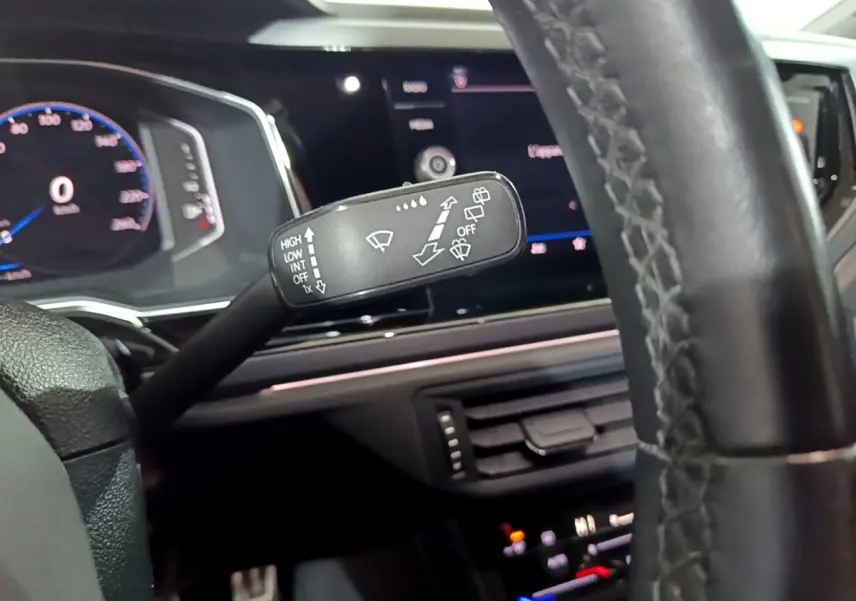 Gros plan sur le commodo d’essuie-glace dans l’habitacle noir du Volkswagen Taigo blanc, tableau de bord numérique en arrière-plan.