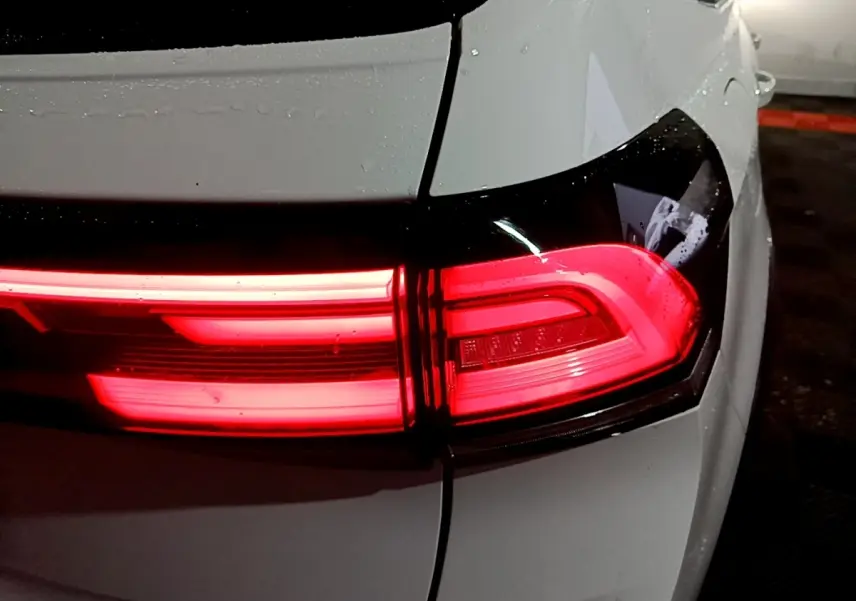 Gros plan sur le feu arrière droit rouge d’un Volkswagen Taigo blanc, version 2022, dans un parking sombre.