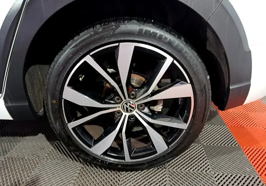Gros plan sur la roue avant droite d’un Volkswagen Taigo blanc, jante alliage bicolore noir et argent.