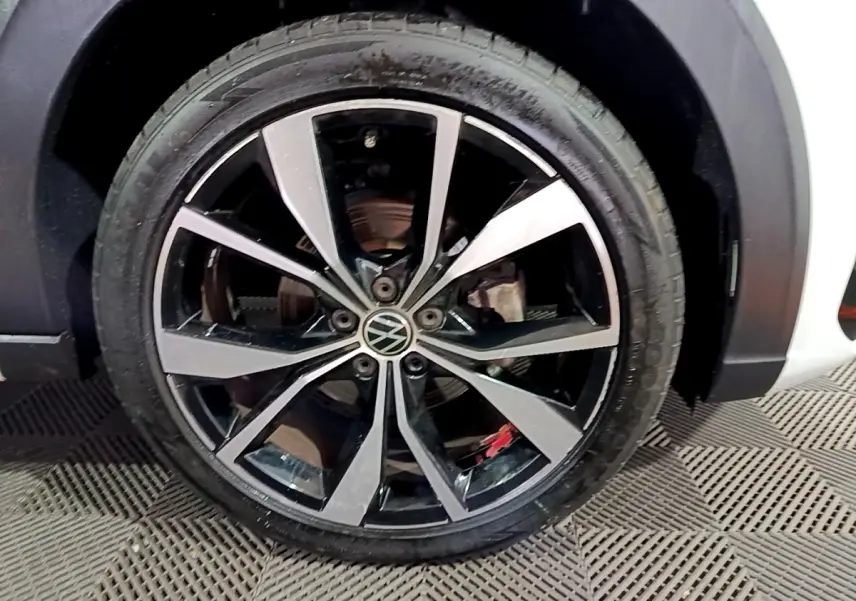 Gros plan sur la roue avant droite du Volkswagen Taigo blanc, jante alliage noir et argentée avec logo VW central.