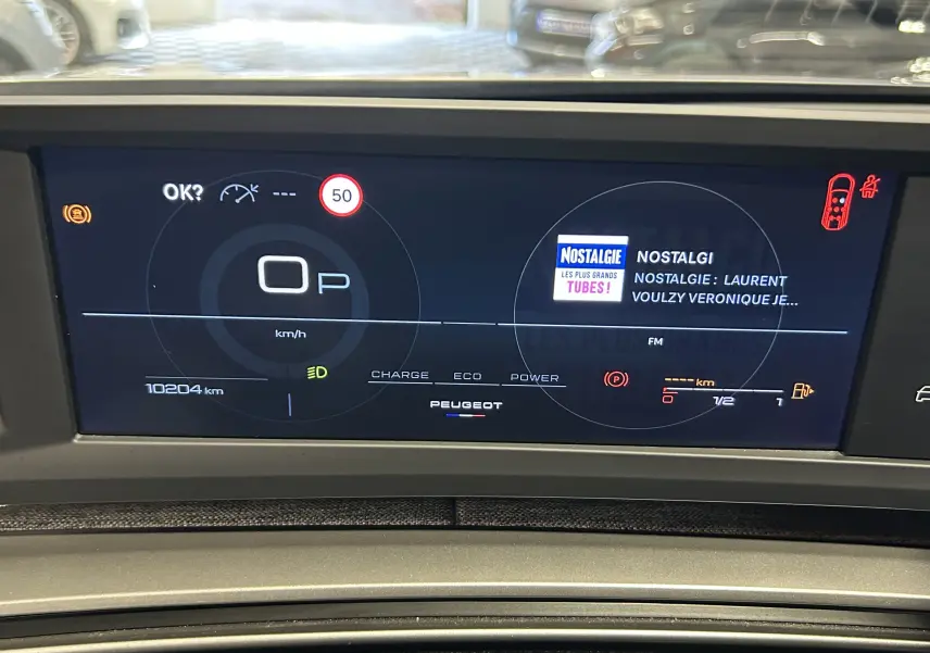 Affichage numérique du tableau de bord Peugeot 5008 hybride 2025, montrant vitesse à 0 km/h et radio Nostalgie.