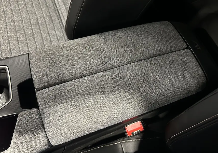 Gros plan sur l'accoudoir central en tissu gris à motifs, intérieur du Peugeot 5008 III Hybrid 2025.