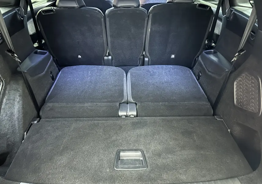 Vue du coffre arrière du Peugeot 5008 hybride 2025 avec sièges rabattus et revêtement intérieur noir.